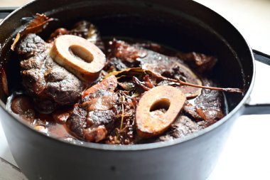 Kırmızı şarapla pişirilmiş kemikli yumuşak sığır eti, taze otlar ve tek bir kırsal siyah tencerede kök sebzelerle servis edilir. Zengin sos ve yavaş pişirilmiş malzemeler geleneksel bir konforlu yemek yemeğinin altını çiziyor..