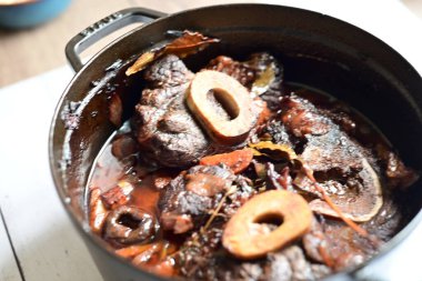 Kırmızı şarapla pişirilmiş kemikli yumuşak sığır eti, taze otlar ve tek bir kırsal siyah tencerede kök sebzelerle servis edilir. Zengin sos ve yavaş pişirilmiş malzemeler geleneksel bir konforlu yemek yemeğinin altını çiziyor..