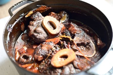 Kırmızı şarapla pişirilmiş kemikli yumuşak sığır eti, taze otlar ve tek bir kırsal siyah tencerede kök sebzelerle servis edilir. Zengin sos ve yavaş pişirilmiş malzemeler geleneksel bir konforlu yemek yemeğinin altını çiziyor..