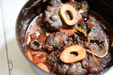 Kırmızı şarapla pişirilmiş kemikli yumuşak sığır eti, taze otlar ve tek bir kırsal siyah tencerede kök sebzelerle servis edilir. Zengin sos ve yavaş pişirilmiş malzemeler geleneksel bir konforlu yemek yemeğinin altını çiziyor..