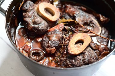 Kırmızı şarapla pişirilmiş kemikli yumuşak sığır eti, taze otlar ve tek bir kırsal siyah tencerede kök sebzelerle servis edilir. Zengin sos ve yavaş pişirilmiş malzemeler geleneksel bir konforlu yemek yemeğinin altını çiziyor..