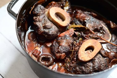 Kırmızı şarapla pişirilmiş kemikli yumuşak sığır eti, taze otlar ve tek bir kırsal siyah tencerede kök sebzelerle servis edilir. Zengin sos ve yavaş pişirilmiş malzemeler geleneksel bir konforlu yemek yemeğinin altını çiziyor..