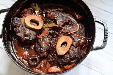 Kırmızı şarapla pişirilmiş kemikli yumuşak sığır eti, taze otlar ve tek bir kırsal siyah tencerede kök sebzelerle servis edilir. Zengin sos ve yavaş pişirilmiş malzemeler geleneksel bir konforlu yemek yemeğinin altını çiziyor..