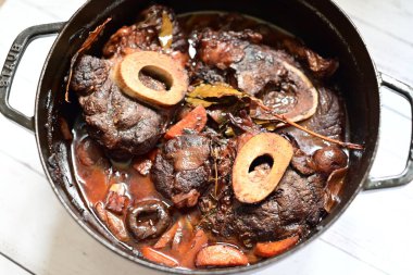 Kırmızı şarapla pişirilmiş kemikli yumuşak sığır eti, taze otlar ve tek bir kırsal siyah tencerede kök sebzelerle servis edilir. Zengin sos ve yavaş pişirilmiş malzemeler geleneksel bir konforlu yemek yemeğinin altını çiziyor..