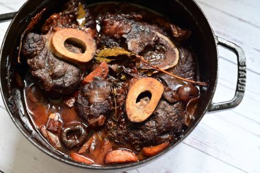 Kırmızı şarapla pişirilmiş kemikli yumuşak sığır eti, taze otlar ve tek bir kırsal siyah tencerede kök sebzelerle servis edilir. Zengin sos ve yavaş pişirilmiş malzemeler geleneksel bir konforlu yemek yemeğinin altını çiziyor..