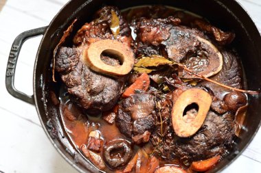 Kırmızı şarapla pişirilmiş kemikli yumuşak sığır eti, taze otlar ve tek bir kırsal siyah tencerede kök sebzelerle servis edilir. Zengin sos ve yavaş pişirilmiş malzemeler geleneksel bir konforlu yemek yemeğinin altını çiziyor..