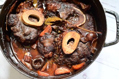 Kırmızı şarapla pişirilmiş kemikli yumuşak sığır eti, taze otlar ve tek bir kırsal siyah tencerede kök sebzelerle servis edilir. Zengin sos ve yavaş pişirilmiş malzemeler geleneksel bir konforlu yemek yemeğinin altını çiziyor..