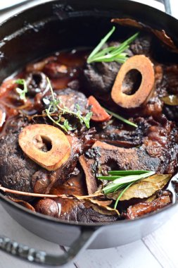 Yanında taze patates, kök sebze ve taze otlarla birlikte kırmızı şarap soslu kemikli haşlanmış sığır eti servis edilir. Beyaz bir tabakta parlak bir arkaplanda sunulan bu çanak, klasik konforlu yiyecekleri inceliyor.