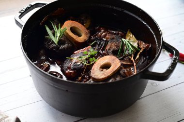 Beyaz bir tabakta renkli sebzelerle servis edilen kemikli kızarmış sığır eti. Tabakta yumuşak, fırında kızartılmış et ve mevsimlik sebzeler yer alıyor ve temiz ve minimalist bir şekilde sunuluyor.