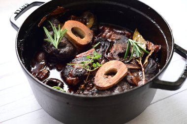 Beyaz bir tabakta renkli sebzelerle servis edilen kemikli kızarmış sığır eti. Tabakta yumuşak, fırında kızartılmış et ve mevsimlik sebzeler yer alıyor ve temiz ve minimalist bir şekilde sunuluyor.