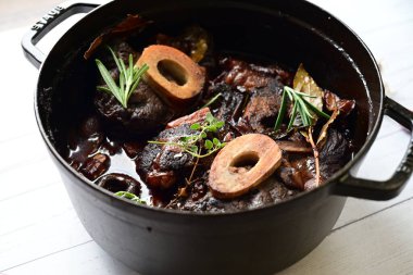 Beyaz bir tabakta renkli sebzelerle servis edilen kemikli kızarmış sığır eti. Tabakta yumuşak, fırında kızartılmış et ve mevsimlik sebzeler yer alıyor ve temiz ve minimalist bir şekilde sunuluyor.