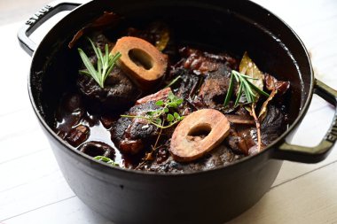 Beyaz bir tabakta renkli sebzelerle servis edilen kemikli kızarmış sığır eti. Tabakta yumuşak, fırında kızartılmış et ve mevsimlik sebzeler yer alıyor ve temiz ve minimalist bir şekilde sunuluyor.