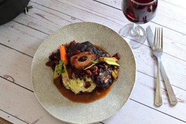 Sebzelerle servis edilen ve taze otlarla süslenen sığır eti osso buco 'sunun yakın çekimi. Kemik iliğiyle pişirilmiş yumuşak et, bu geleneksel İtalyan yemeğinin dokusunu ve derinliğini vurguluyor. 