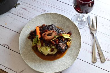 Sebzelerle servis edilen ve taze otlarla süslenen sığır eti osso buco 'sunun yakın çekimi. Kemik iliğiyle pişirilmiş yumuşak et, bu geleneksel İtalyan yemeğinin dokusunu ve derinliğini vurguluyor. 