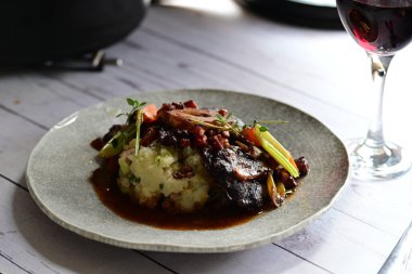 Sebzelerle servis edilen ve taze otlarla süslenen sığır eti osso buco 'sunun yakın çekimi. Kemik iliğiyle pişirilmiş yumuşak et, bu geleneksel İtalyan yemeğinin dokusunu ve derinliğini vurguluyor. 