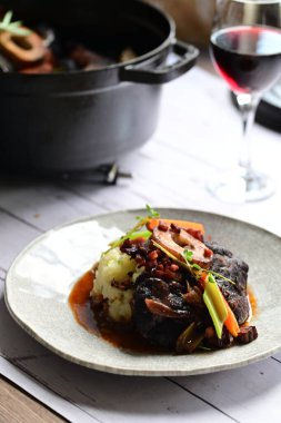 Sebzelerle servis edilen ve taze otlarla süslenen sığır eti osso buco 'sunun yakın çekimi. Kemik iliğiyle pişirilmiş yumuşak et, bu geleneksel İtalyan yemeğinin dokusunu ve derinliğini vurguluyor. 