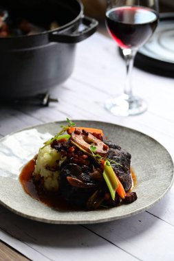 Sebzelerle servis edilen ve taze otlarla süslenen sığır eti osso buco 'sunun yakın çekimi. Kemik iliğiyle pişirilmiş yumuşak et, bu geleneksel İtalyan yemeğinin dokusunu ve derinliğini vurguluyor. 