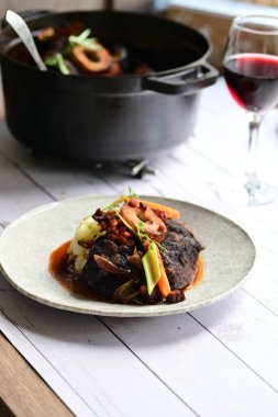 Sebzelerle servis edilen ve taze otlarla süslenen sığır eti osso buco 'sunun yakın çekimi. Kemik iliğiyle pişirilmiş yumuşak et, bu geleneksel İtalyan yemeğinin dokusunu ve derinliğini vurguluyor. 