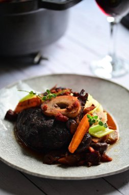 Sebzelerle servis edilen ve taze otlarla süslenen sığır eti osso buco 'sunun yakın çekimi. Kemik iliğiyle pişirilmiş yumuşak et, bu geleneksel İtalyan yemeğinin dokusunu ve derinliğini vurguluyor. 