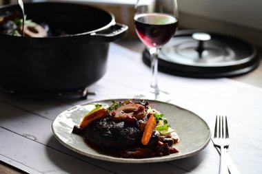 Yanında taze patates, kök sebze ve taze otlarla birlikte kırmızı şarap soslu kemikli haşlanmış sığır eti servis edilir..