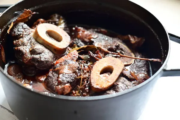 Kırmızı şarapla pişirilmiş kemikli yumuşak sığır eti, taze otlar ve tek bir kırsal siyah tencerede kök sebzelerle servis edilir. Zengin sos ve yavaş pişirilmiş malzemeler geleneksel bir konforlu yemek yemeğinin altını çiziyor..