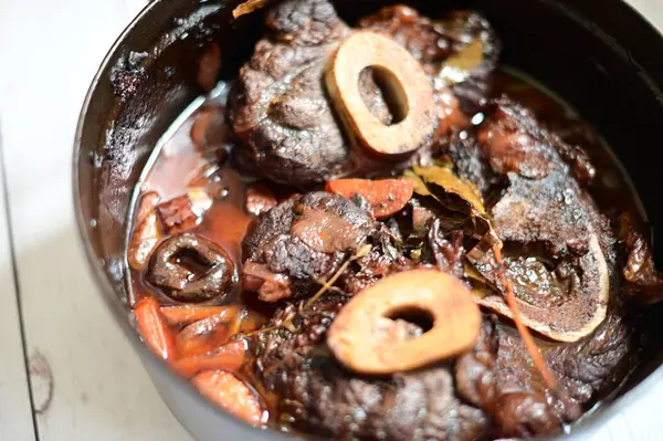 Kırmızı şarapla pişirilmiş kemikli yumuşak sığır eti, taze otlar ve tek bir kırsal siyah tencerede kök sebzelerle servis edilir. Zengin sos ve yavaş pişirilmiş malzemeler geleneksel bir konforlu yemek yemeğinin altını çiziyor..