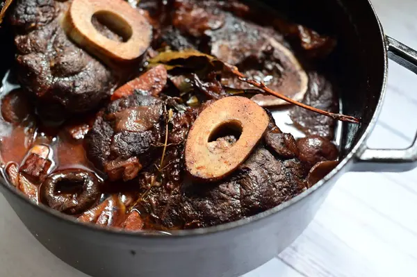 Kırmızı şarapla pişirilmiş kemikli yumuşak sığır eti, taze otlar ve tek bir kırsal siyah tencerede kök sebzelerle servis edilir. Zengin sos ve yavaş pişirilmiş malzemeler geleneksel bir konforlu yemek yemeğinin altını çiziyor..