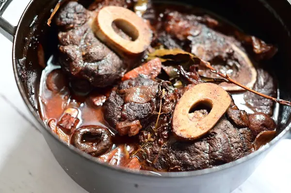 Kırmızı şarapla pişirilmiş kemikli yumuşak sığır eti, taze otlar ve tek bir kırsal siyah tencerede kök sebzelerle servis edilir. Zengin sos ve yavaş pişirilmiş malzemeler geleneksel bir konforlu yemek yemeğinin altını çiziyor..