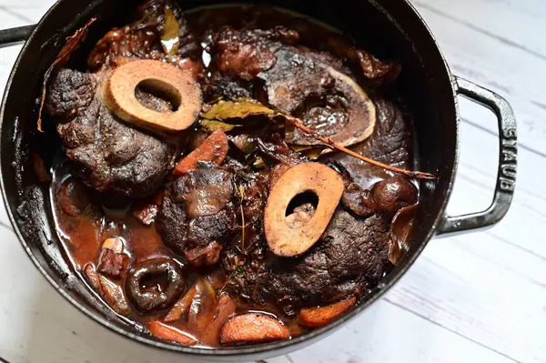 Kırmızı şarapla pişirilmiş kemikli yumuşak sığır eti, taze otlar ve tek bir kırsal siyah tencerede kök sebzelerle servis edilir. Zengin sos ve yavaş pişirilmiş malzemeler geleneksel bir konforlu yemek yemeğinin altını çiziyor..