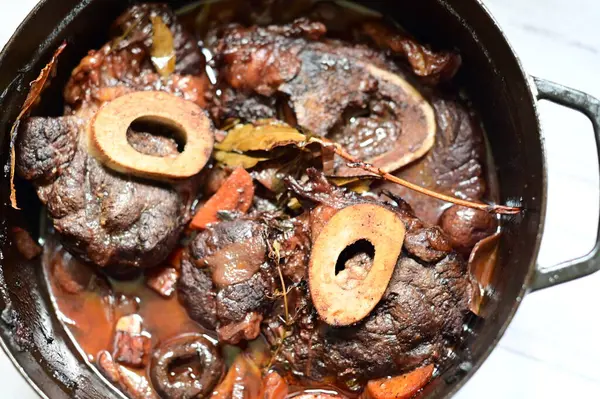 Kırmızı şarapla pişirilmiş kemikli yumuşak sığır eti, taze otlar ve tek bir kırsal siyah tencerede kök sebzelerle servis edilir. Zengin sos ve yavaş pişirilmiş malzemeler geleneksel bir konforlu yemek yemeğinin altını çiziyor..