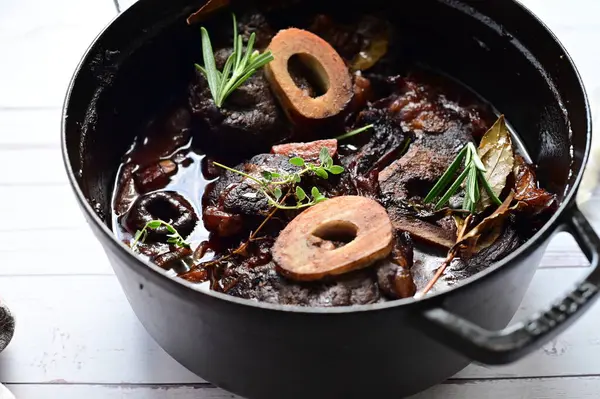 Beyaz bir tabakta renkli sebzelerle servis edilen kemikli kızarmış sığır eti. Tabakta yumuşak, fırında kızartılmış et ve mevsimlik sebzeler yer alıyor ve temiz ve minimalist bir şekilde sunuluyor.