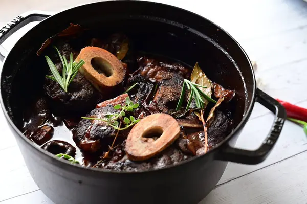 Beyaz bir tabakta renkli sebzelerle servis edilen kemikli kızarmış sığır eti. Tabakta yumuşak, fırında kızartılmış et ve mevsimlik sebzeler yer alıyor ve temiz ve minimalist bir şekilde sunuluyor.