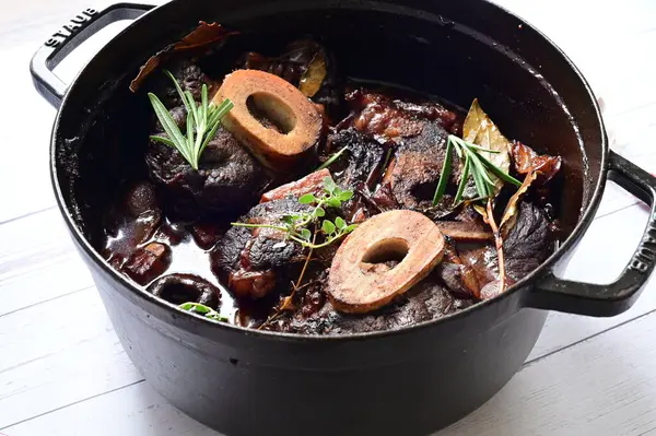 Beyaz bir tabakta renkli sebzelerle servis edilen kemikli kızarmış sığır eti. Tabakta yumuşak, fırında kızartılmış et ve mevsimlik sebzeler yer alıyor ve temiz ve minimalist bir şekilde sunuluyor.