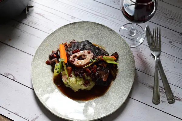 Sebzelerle servis edilen ve taze otlarla süslenen sığır eti osso buco 'sunun yakın çekimi. Kemik iliğiyle pişirilmiş yumuşak et, bu geleneksel İtalyan yemeğinin dokusunu ve derinliğini vurguluyor. 