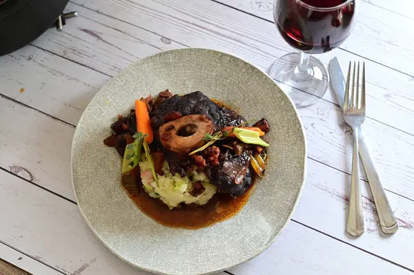 Sebzelerle servis edilen ve taze otlarla süslenen sığır eti osso buco 'sunun yakın çekimi. Kemik iliğiyle pişirilmiş yumuşak et, bu geleneksel İtalyan yemeğinin dokusunu ve derinliğini vurguluyor. 