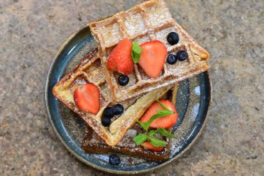 Koyu ahşap masada çilekli Belçika waffleları, nane ve yaban mersini.