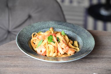 Masadaki siyah tabakta karides ve domatesli makarna.