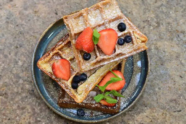 Koyu ahşap masada çilekli Belçika waffleları, nane ve yaban mersini.