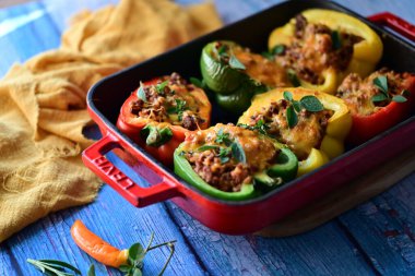 Renkli çan biberlerinin üst görüntüsü. İçi öğütülmüş et, pilav ve karışık sebzelerle doldurulmuş. Seramik bir fırın kabına dizilmiş.. 