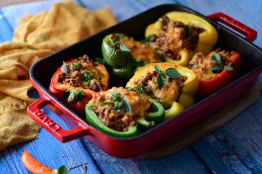 Renkli çan biberlerinin üst görüntüsü. İçi öğütülmüş et, pilav ve karışık sebzelerle doldurulmuş. Seramik bir fırın kabına dizilmiş.. 