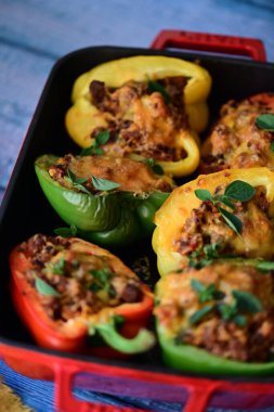 Renkli çan biberlerinin üst görüntüsü. İçi öğütülmüş et, pilav ve karışık sebzelerle doldurulmuş. Seramik bir fırın kabına dizilmiş.. 