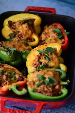 Renkli çan biberlerinin üst görüntüsü. İçi öğütülmüş et, pilav ve karışık sebzelerle doldurulmuş. Seramik bir fırın kabına dizilmiş.. 