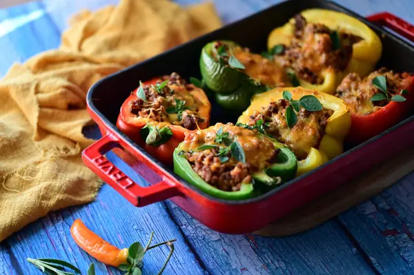 Renkli çan biberlerinin üst görüntüsü. İçi öğütülmüş et, pilav ve karışık sebzelerle doldurulmuş. Seramik bir fırın kabına dizilmiş.. 