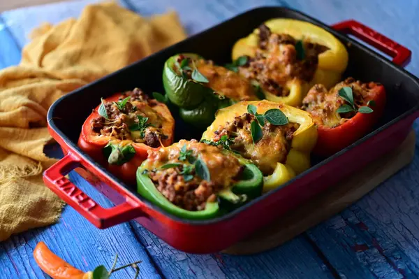 Renkli çan biberlerinin üst görüntüsü. İçi öğütülmüş et, pilav ve karışık sebzelerle doldurulmuş. Seramik bir fırın kabına dizilmiş.. 