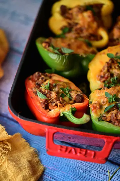 Renkli çan biberlerinin üst görüntüsü. İçi öğütülmüş et, pilav ve karışık sebzelerle doldurulmuş. Seramik bir fırın kabına dizilmiş.. 