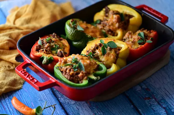 Doldurulmuş biber, et, peynir ve sebzeler, mavi ahşap bir arka planda kızartma tavasında..