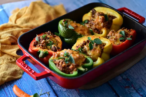 Doldurulmuş biber, et, peynir ve sebzeler, mavi ahşap bir arka planda kızartma tavasında..