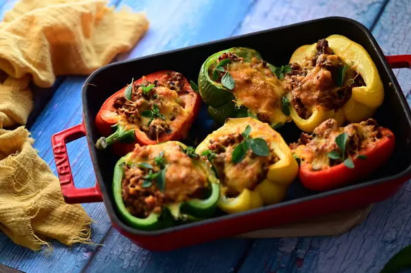 Doldurulmuş biber, et, peynir ve sebzeler, mavi ahşap bir arka planda kızartma tavasında..