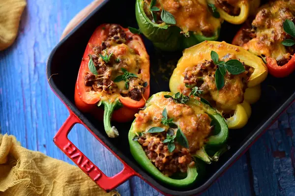 Doldurulmuş biber, et, peynir ve sebzeler, mavi ahşap bir arka planda kızartma tavasında..