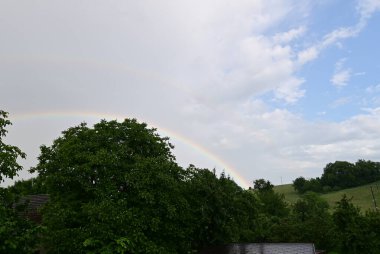Gökkuşağı yeşil tarlanın üzerinde bir ev ve mavi bir gökyüzü.